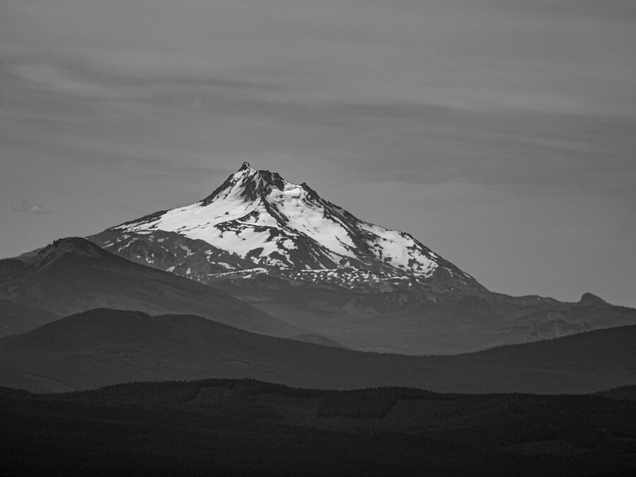 A snow-capped peak rises beyond layered dark ridges in black and white.