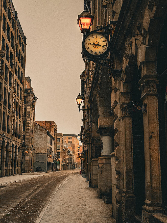 An ornate street clock overlooks a quiet street lined with historic buildings.